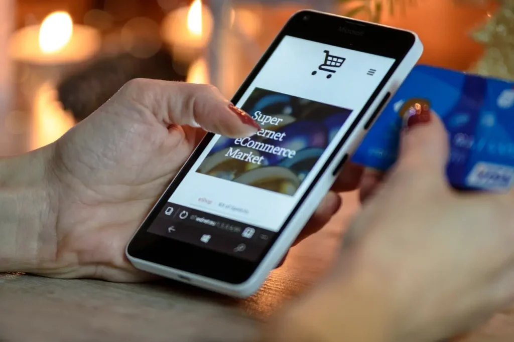 A person using a smartphone for online shopping while holding a credit card, representing digital spending habits and the need for modern budgeting tools to manage finances effectively.
