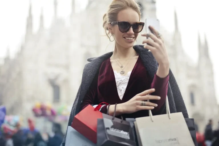 A stylish woman holding multiple shopping bags and taking a selfie, representing emotional spending habits and impulsive shopping behavior.