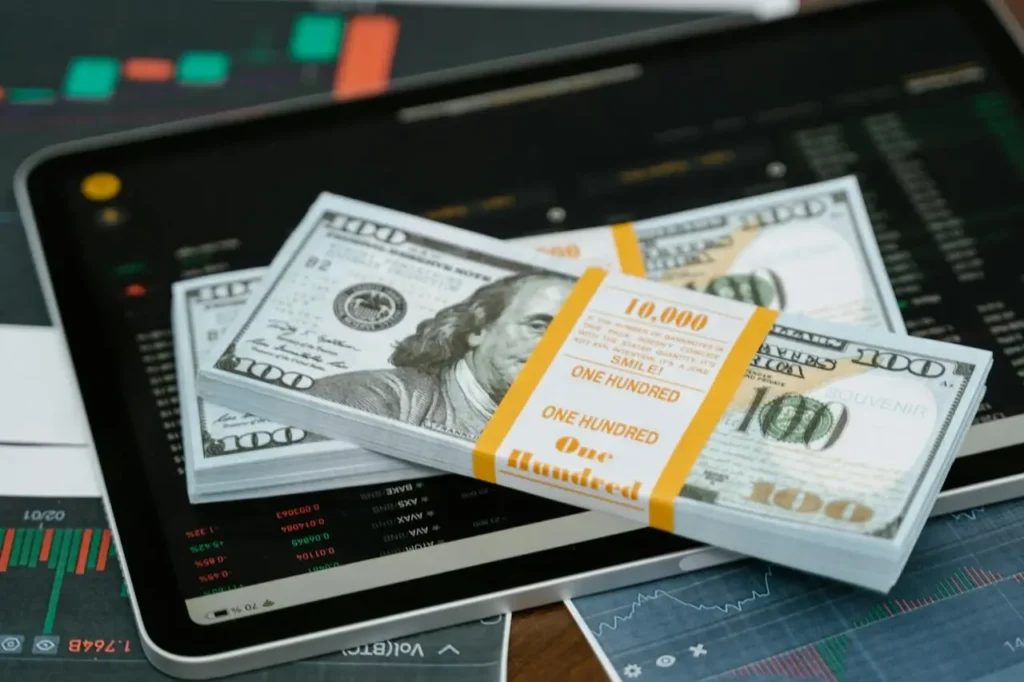 Stacks of U.S. dollar bills placed on a tablet displaying financial market charts, symbolizing ways to grow your wealth without a traditional job.